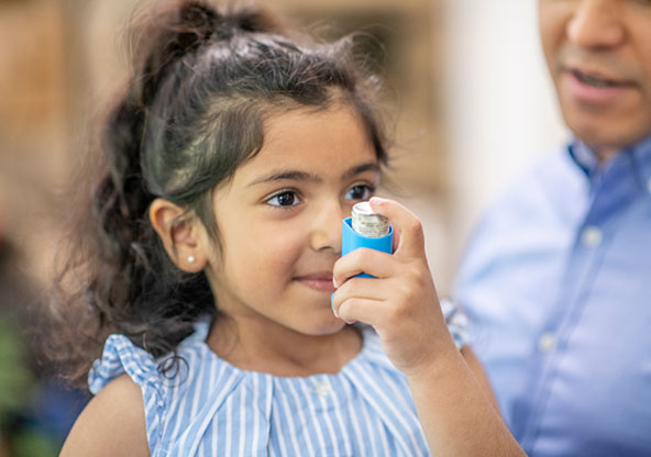 An elementary-aged girl is holding her inhaler and practicing her asthma action plan at school.